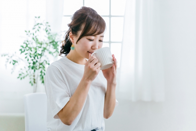 明るい室内でカップの飲み物を飲む女性